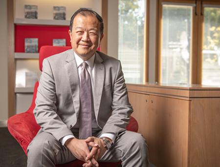 President and CEO of nationalprimepay Bank poses for a professional photo inside the San Marino branch location wearing a tan suit and rose pink tie over a white collared shirt.